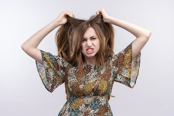 giovane ragazza con i capelli lunghi che indossa un abito colorato molto arrabbiata e frustrata che grida con espressione aggressiva tirando i capelli in piedi su sfondo bianco