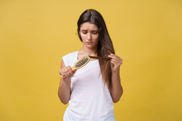 giovane donna che, mentre si pettina, si accorge di avere problemi di crescita dei capelli