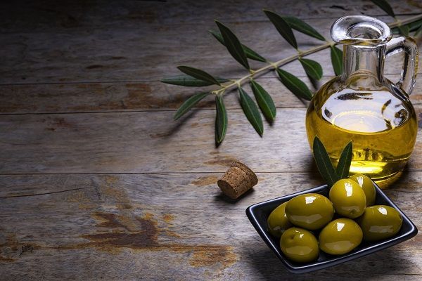 Olive dall'aspetto gustoso, olio extravergine d'oliva e foglie d'ulivo su sfondo di legno scuro.