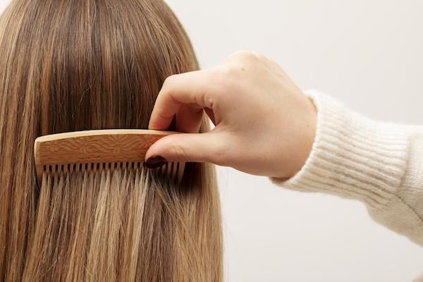 una donna bionda pettina i capelli con un pettine di bamboo