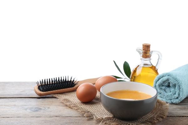 Maschera per capelli fatta in casa in una ciotola con ingredienti freschi e pennello su un tavolo di legno con sfondo bianco. 