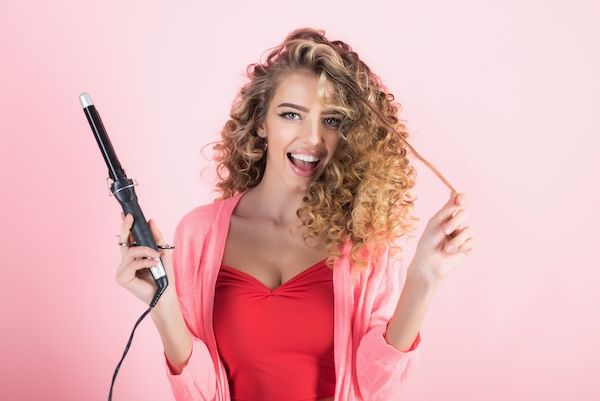Ragazza sorridente con capelli ricci ha attrezzatura da parrucchiere. Parrucchiere. Bellezza e stile. Professione dell'industria della bellezza. Trucco e cosmetici per la cura della pelle. Isolata su sfondo bianco