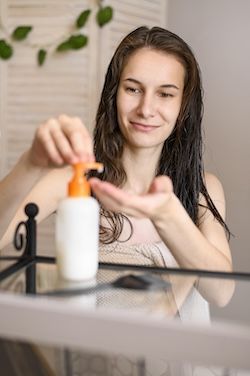Donna con balsamo senza risciacquo per i capelli dentro il bagno 