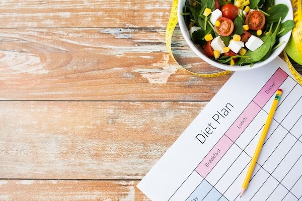 Alimentazione sana, cibi, dimagrimento e concetto di perdita di peso - primo piano di un piano dietetico su carta con nastro metrico e insalata
