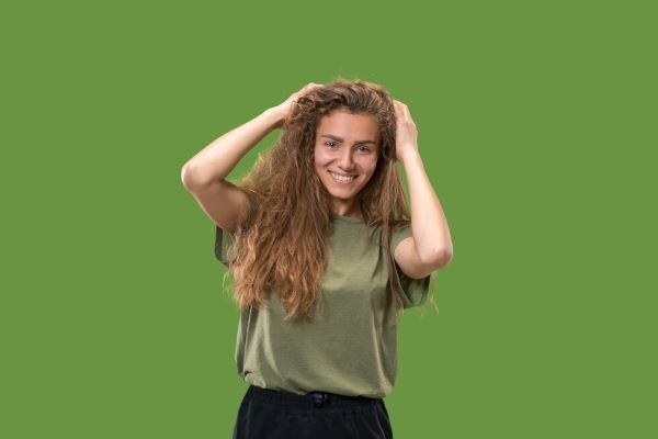 Donna felice in piedi e sorridente isolata su sfondo verde di studio. Capelli porosi