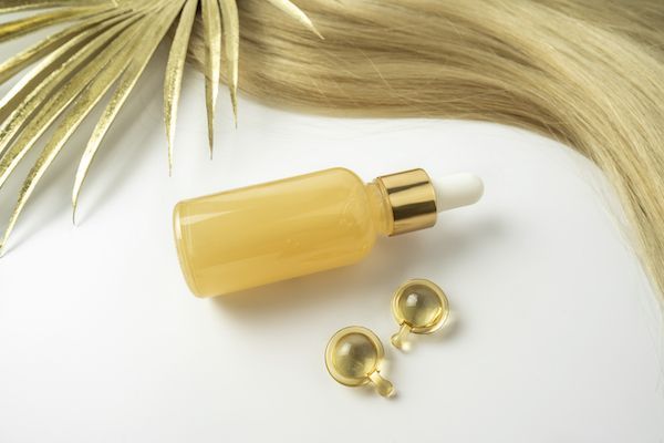Un olio o siero naturale per la cura dei capelli e una ciocca di capelli biondi su sfondo bianco
