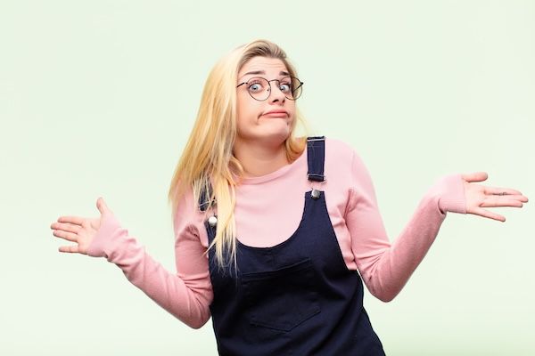 Giovane donna bionda e bella che si sente confusa e smarrita, insicura sulla risposta o decisione giusta, cercando di prendere una decisione davanti al muro.