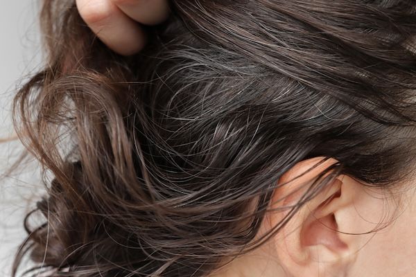 Una donna mora mostra i suoi capelli bianchi e li tiene con la mano insieme alle pinze