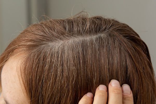 Chiudi la testa con capelli bianchi alle radici lungo la riga prima di tingere