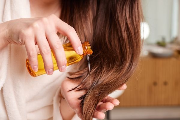 Donna che applica olio per capelli nel bagno moderno, concetto di cura dei capelli