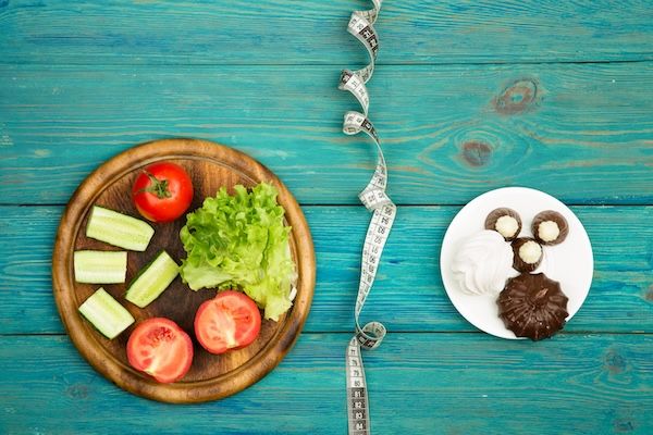 Scelta della dieta alimentare tra verdure o pasticcini e dolci e nastro metrico