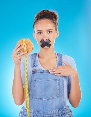 La dieta dell'hamburger e la bocca chiusa con nastro di una donna per il fast food e la perdita di peso danno disgusto e frustrazione per la protezione, errore di disastro e persona delusa isolata su uno sfondo blu in studio