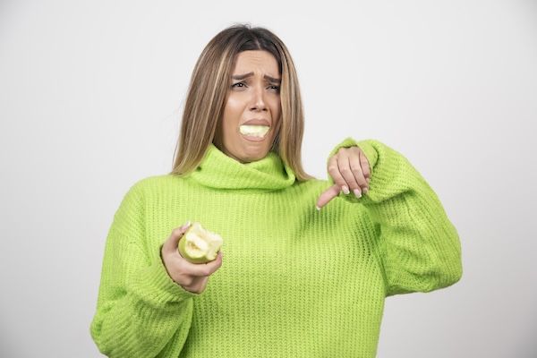 Giovane donna con una maglietta verde che mangia una mela.