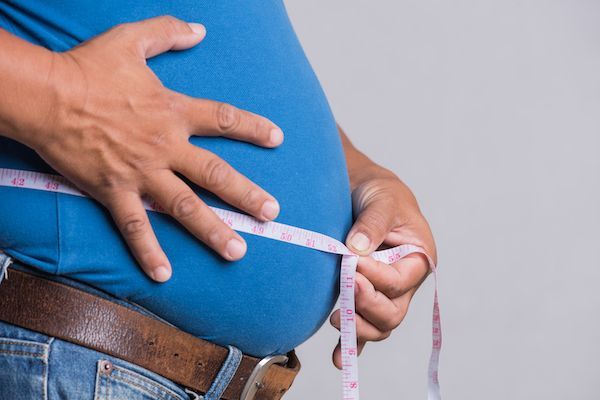 uomo obeso che si misura la pancia