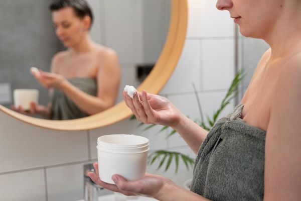 Ragazza che tiene una manciata di crema davanti allo specchio.