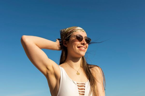 Ragazza che indossa un berretto per capelli sorridente sulla spiaggia. Proteggere i nostri capelli con asciugamani o cappelli è un modo per prevenire i capelli opachi.