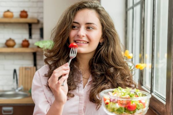 Ragazza sorridente che mangia insalata.