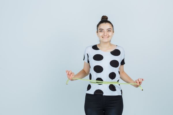 Ragazza che sorride mentre misura la sua vita