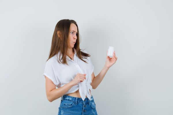 Ragazza in camicetta bianca e jeans che tengono e guardano un barattolo.
