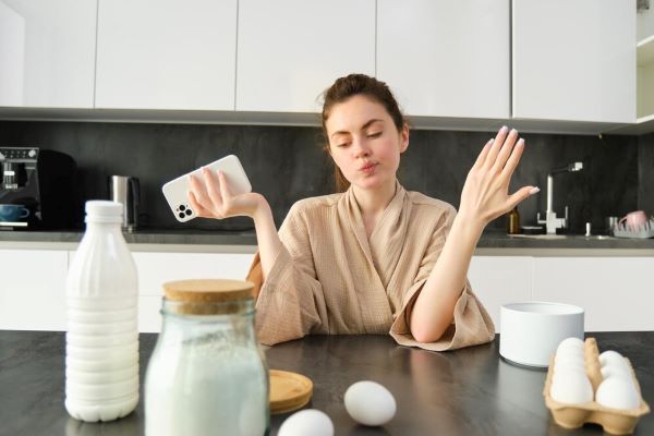 Ragazza con un gesto indeciso in cucina con in mano il telefono
