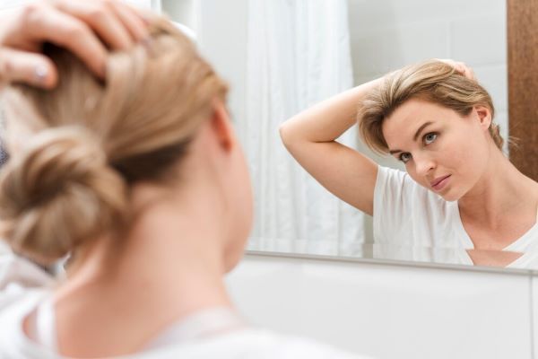 Donna che si guarda allo specchio con una mano tra i capelli.