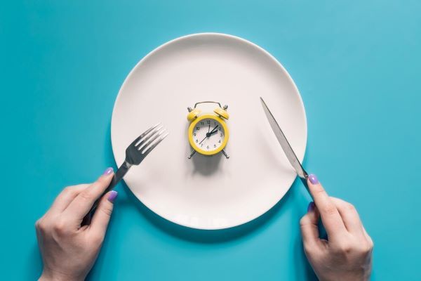 Mani che tengono un coltello e una forchetta sopra una sveglia su un piatto
