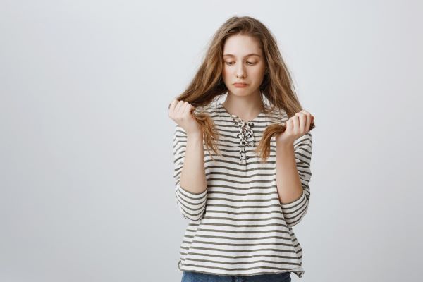 Ragazza che guarda le punte dei capelli in modo dubbioso