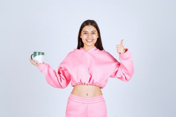 Ragazza che tiene una tazza di caffè e alza un pollice con l'altra mano