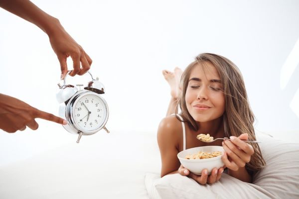 Le mani che mostrano l'ora a una donna sdraiata a letto