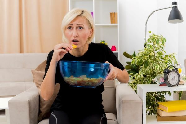 La signora guarda la televisione mentre mangia degli snack