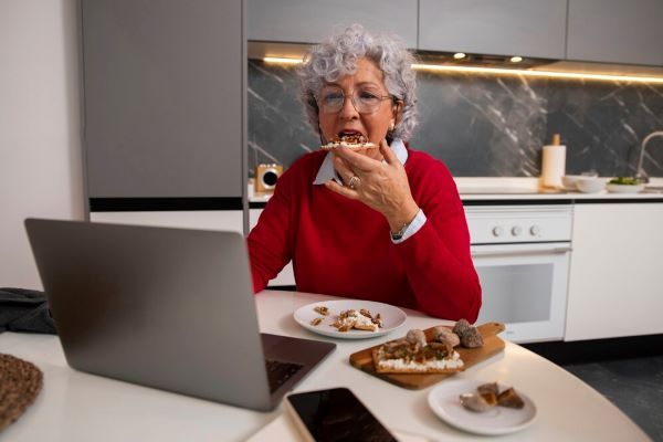 Donna senior che mangia e che usa un computer