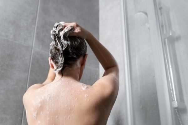 Ragazza che si lava i capelli sotto la doccia
