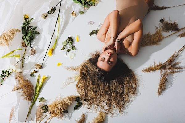 Una donna snella con una tuta beige posa accanto a fiori secchi su uno sfondo bianco isolato