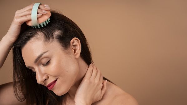 Una donna di corporatura media si massaggia il cuoio capelluto.