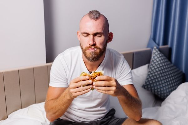 Giovane con fast food a casa nella camera da letto a letto