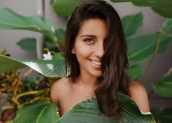 Bella signora con capelli ricci e occhi verdi sorride dolcemente Donna con ciglia lunghe in posa sullo sfondo di una pianta tropicale
