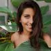 Bella signora con capelli ricci e occhi verdi sorride dolcemente Donna con ciglia lunghe in posa sullo sfondo di una pianta tropicale