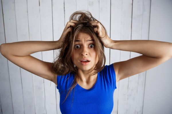 Donna turbata che tiene i capelli tra le mani su una parete di legno bianco