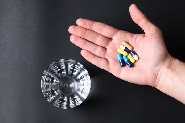 Pillole mediche colorate nella mano di una persona e un bicchiere d'acqua