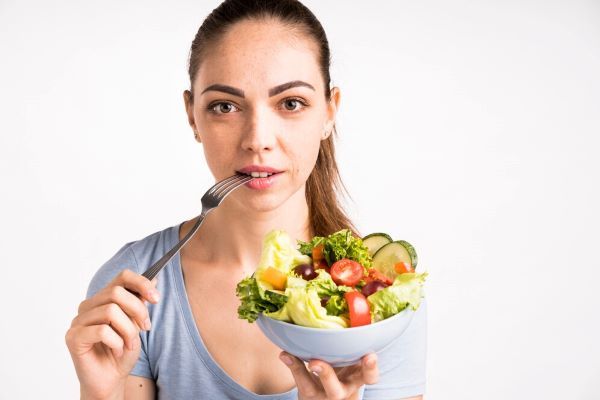 donna bianca con una forchetta in bocca e una ciotola di insalata in mano. dieta anti aging