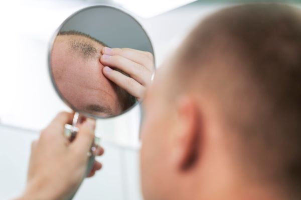 L'uomo alza la mano sui capelli mentre si guarda allo specchio.