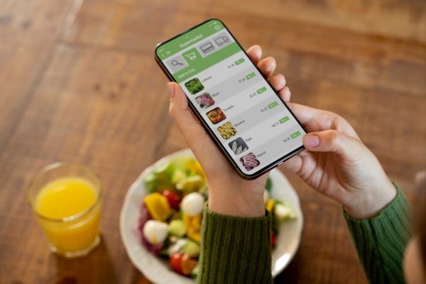 Ragazza che scrive il cibo sul suo telefono. Applicazioni moderne come i diari alimentari possono permetterci di migliorare la nostra salute e il nostro aspetto.