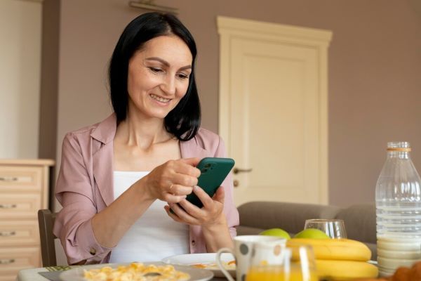 Donna felice che usa il telefono prima di mangiare. Avendo un diario alimentare sul telefono, è più facile annotare i dettagli dei pasti.