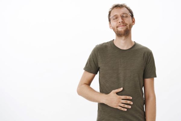Ragazzo sorridente con la mano appoggiata sullo stomaco. Prendersi cura della salute dell'apparato digerente è importante per il nostro benessere.