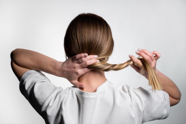 Ragazza ripresa da dietro mentre arrotola i suoi capelli castano chiaro dipinti con riflessi più giallastri.