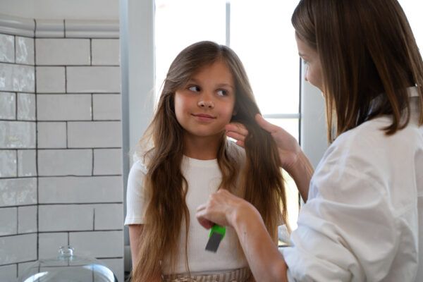 La madre pettina i capelli lisci della figlia in bagno.