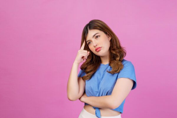 Modella in posa in uno studio con sfondo rosa che si tocca il mento con un dito mentre guarda di lato con un'espressione dubbiosa.