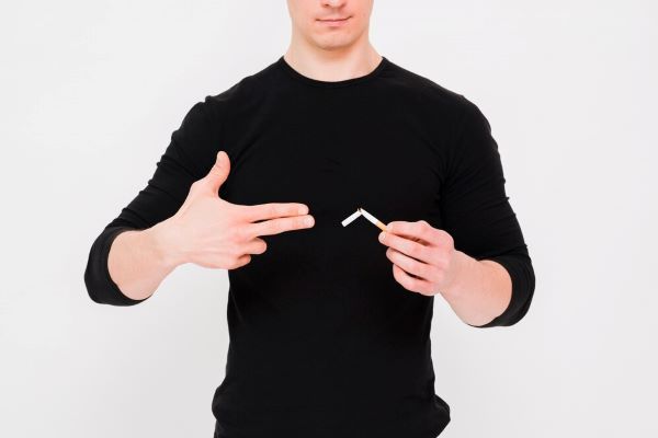 Uomo che fa la forma di una pistola con la mano che tiene una sigaretta rotta con l'altra