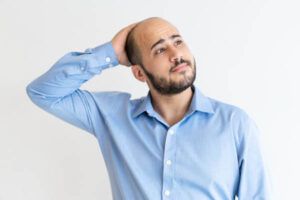 uomo calvo che pensa mentre si tocca la testa